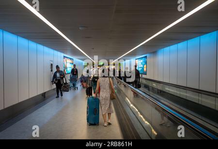 Une femme pousse une valise roulante bleue à côté d'un voyageur aux départs au terminal sud de l'aéroport de Gatwick, Londres, Royaume-Uni. Banque D'Images