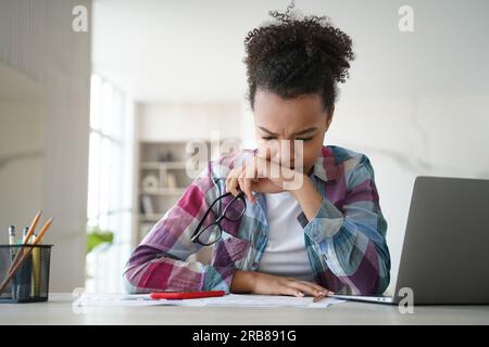 Pensif étudiant biracial se prépare diligemment aux examens, étudiant à domicile. Fatigué mais concentré, engagé dans l'enseignement à distance. Banque D'Images