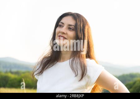 Portrait d'une femme pensive de 35 ans dans un T-shirt blanc contre le ciel dans la nature en été. Banque D'Images