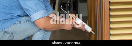 Image des mains d'un bricoleur qui, avec un pistolet en silicone, installe et scelle les portes et les fenêtres contre les courants d'air. Améliorations de l'isolation thermique d'une maison. Banque D'Images