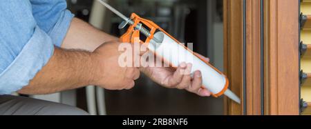 Image des mains d'un bricoleur qui, avec un pistolet en silicone, installe et scelle les portes et les fenêtres contre les courants d'air. Améliorations de l'isolation thermique d'une maison. Banque D'Images