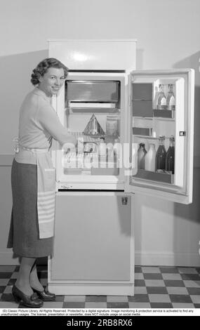 Dans la cuisine 1960s. Une femme dans sa cuisine avec la porte du réfrigérateur ouverte. Vous pouvez voir les produits alimentaires de différentes sortes qui sont soigneusement affichés sur les étagères. Entre autres choses, le paquet classique de lait Tetran est visible. Inventé par Ruben Rausing et qui est devenu le début de l'empire de l'emballage Tetra Pak. Suède 1960. Conard réf. 4188 Banque D'Images