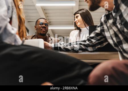 Bon employé noir de sexe masculin face à des idées avec son collègue de Ginger. Sa collègue brune le regarde Banque D'Images
