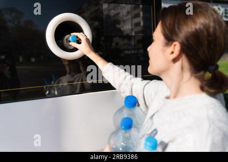 La femme utilise une machine en libre-service pour recevoir des bouteilles et des canettes en plastique usagées dans une rue de la ville. Banque D'Images