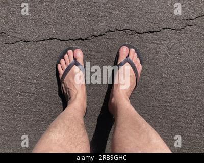 Pieds dans des sandales en caoutchouc marchant sur l'herbe et le sol de terre. Chinelo Havaianas Banque D'Images