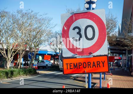 Panneau de limite de vitesse temporaire de 30 km sur une rue commerçante de banlieue animée. Flou panneaux détour avant le long de la route. Travaux routiers sur les routes d'Auckland. Banque D'Images