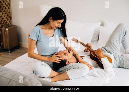 Homme et femme heureux appréciant avec la musique jouant sur instrument, jeune couple jouant de la guitare ukulele à la maison, heureux jeune couple passant du temps ensemble Banque D'Images