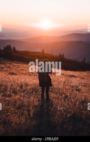 Femme debout et capturant la scène sur un pic de montagne quand le soleil descend, beau coucher de soleil à Krkonose, République Tchèque Banque D'Images