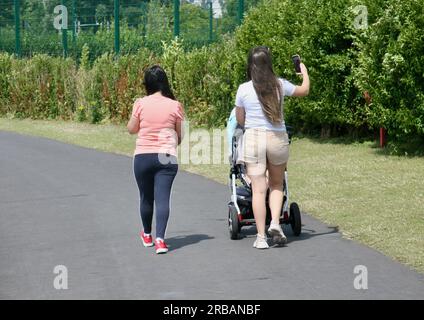 Deux dames marchant dans le parc alors que l'une d'elles prend un selfie sur son téléphone portable Banque D'Images