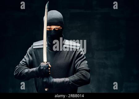 Combat ninja posant avec une épée sur fond noir. concept de combattant japonais Banque D'Images