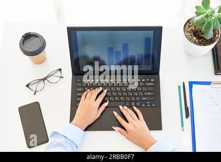 Vue de dessus des mains de femme d'affaires tapant sur un ordinateur portable sur une table de bureau blanche moderne, regardez l'analyse graphique des données statistiques de la finance Banque D'Images