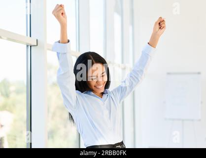 Portrait d'une femme d'affaires noire heureuse et excitée dont les bras sont levés pour célébrer succès dans le bureau créatif moderne Banque D'Images