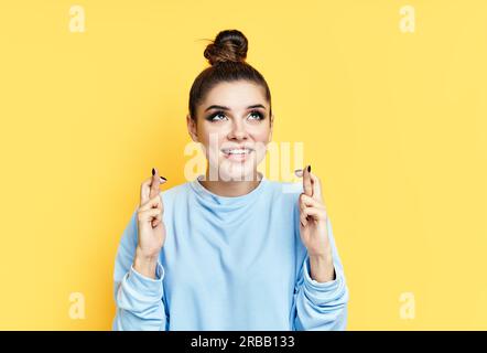 Jeune belle femme croisant ses doigts et souhaitant bonne chance sur fond jaune. Concept espoir et souhait Banque D'Images