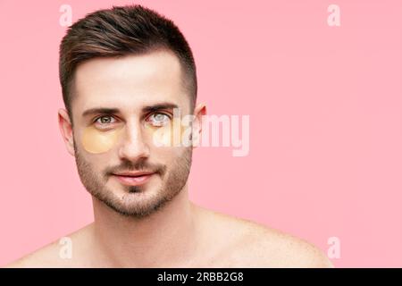 Gros plan portrait de bel homme souriant avec des taches d'oeil d'or sur fond rose. Espace de copie. Beauté masculine, concept de soins de la peau Banque D'Images