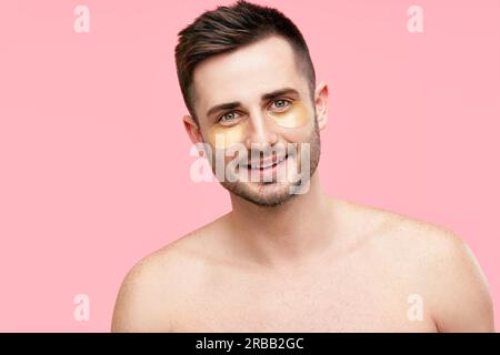 Portrait de bel homme souriant avec des taches d'oeil d'or sur fond rose. Beauté masculine, concept de soins de la peau Banque D'Images