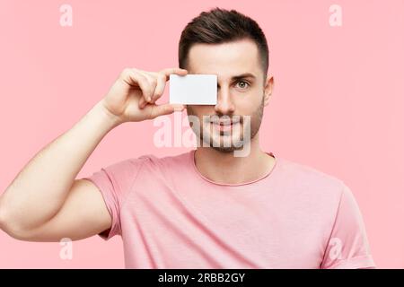 Beau sourire homme tenant la carte de crédit près de son visage fermer l'œil sur fond rose. Shopping, paiement concept Banque D'Images