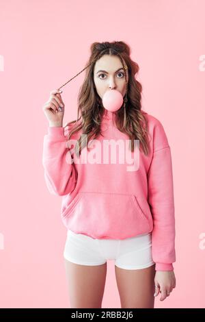 Jeune femme suprisée soufflant de la bulle de la gomme à mâcher sur fond rose Banque D'Images