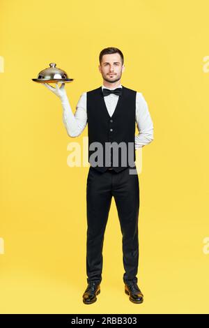 Portrait complet d'un élégant plateau de rangement de serveur avec couvercle prêt à servir sur fond jaune. Restaurant, concept horeca Banque D'Images