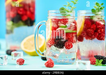 Cocktail de baies fraîches dans un pot en verre. Cocktail d'été frais avec mélange de baies, citron et menthe sur fond bleu. Fête, boisson, concept d'été Banque D'Images