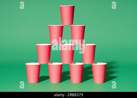 Pyramide de gobelets en papier rouge sur fond vert. Concept de minimalisme Banque D'Images