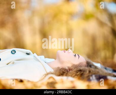 Portrait d'automne d'une jeune femme souriante et heureuse qui se détend dans des feuilles jaunes d'automne avec un espace de copie.Joyeux automne, repos, beauté féminine concept Banque D'Images