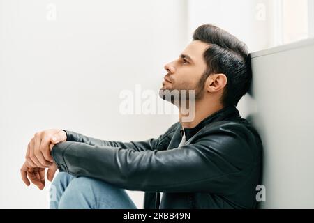 Portrait d'un beau homme attentionné assis sur le sol incliné au mur. La beauté des hommes, le concept des émotions Banque D'Images