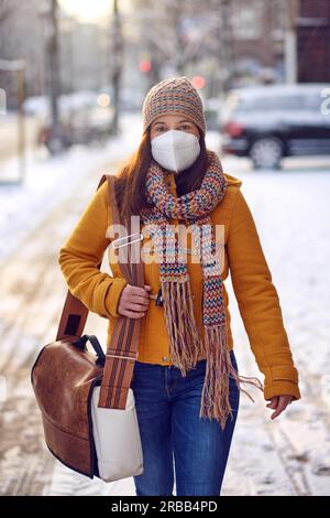 Femme brune d'âge moyen en vêtements d'hiver portant un masque facial à l'extérieur En raison du virus Corona dehors pendant son chemin à travail Banque D'Images