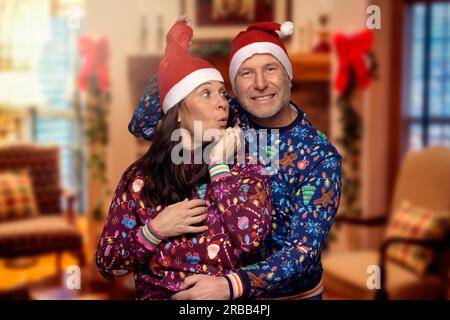 Couple romantique et ludique d'âge moyen dans des vêtements colorés sur le thème de Noël célébrant Noël et la saison des fêtes dans des chapeaux de Père Noël rouges festifs Banque D'Images