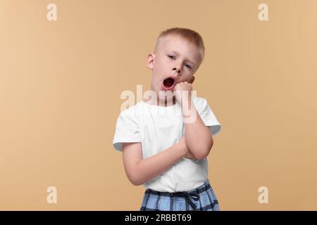 Garçon endormi bâillant sur fond beige. Problème d'insomnie Banque D'Images