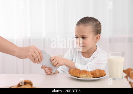 Femme emportant smartphone de sa fille à la table à l'intérieur, gros plan. Addiction à Internet Banque D'Images
