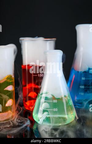 Verrerie de laboratoire avec liquides colorés et vapeur sur fond noir. Réaction chimique Banque D'Images