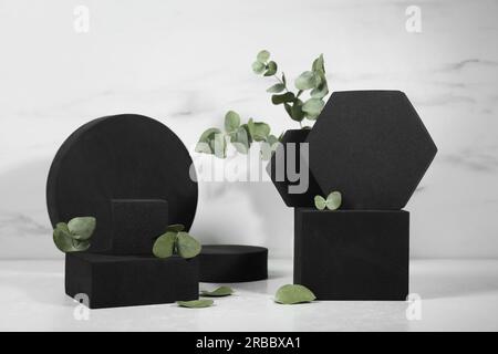 Figurines géométriques noires et feuilles d'eucalyptus sur une table en marbre blanc. Présentation élégante du produit Banque D'Images