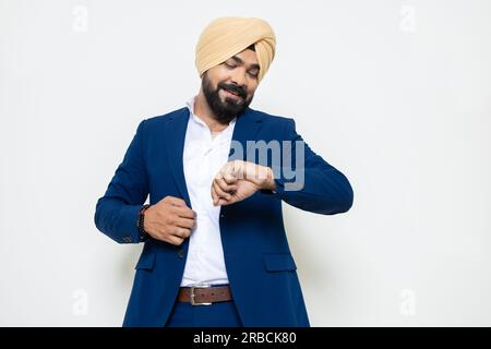 Jeune homme d'affaires sikh indien portant un costume regardant sa montre-bracelet vérifie le temps isolé sur fond blanc. Homme d'entreprise attendant quelqu'un wh Banque D'Images