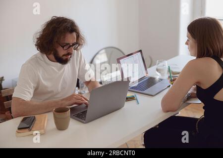 Couple marié indépendants assis à table dans la salle de séjour avec des ordinateurs portables et travaillant à domicile Banque D'Images