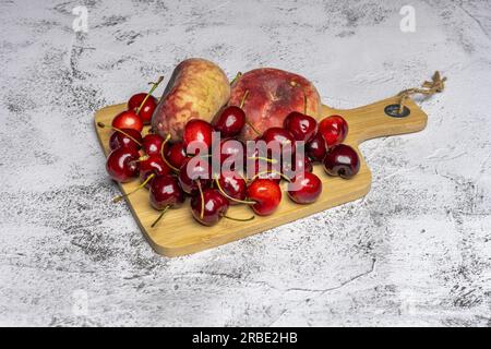 quelques délicieuses cerises mûres et paraguayos sur une planche de cuisine en bambou et sur une surface blanche écaillée Banque D'Images