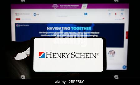 Personne tenant le téléphone portable avec le logo de la société américaine de produits de santé Henry Schein Inc. Sur l'écran devant la page Web. Concentrez-vous sur l'affichage du téléphone. Banque D'Images