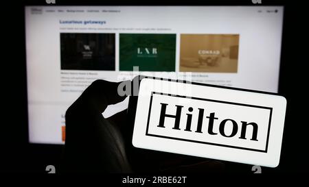 Personne détenant un téléphone portable avec le logo de la société américaine Hilton Worldwide Holdings Inc. Sur l'écran devant la page Web de l'entreprise. Concentrez-vous sur l'affichage du téléphone. Banque D'Images