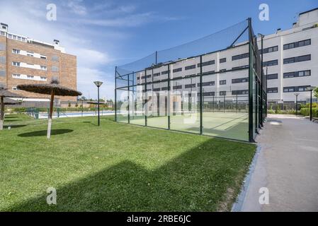 Jardins avec piscine, parasols en paille et court de tennis avec de hautes clôtures métalliques Banque D'Images