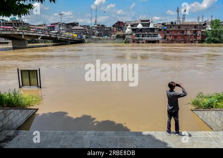 Srinagar, Inde. 09 juillet 2023. Un homme prend des photos alors que la rivière Jehlum est vue couler au-dessus de la marque d'alerte aux inondations suite à des pluies incessantes à Srinagar. Le Jhelum coulait au-dessus de la marque d'alerte aux inondations dans le sud du Cachemire et Srinagar en raison d'un temps nuageux et de la possibilité de nouvelles pluies au cours des prochaines 24 heures. Crédit : SOPA Images Limited/Alamy Live News Banque D'Images