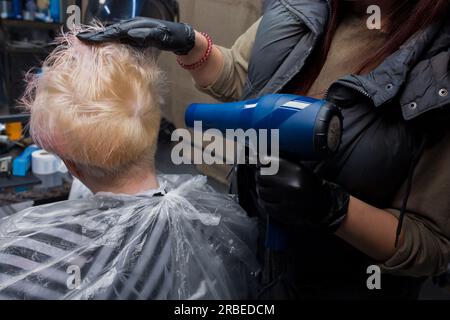 Les mains d'une barbier professionnelle travaillent avec un client, séchent le dos des cheveux de la tête de la femme en cours de coupe et de teinture. Banque D'Images