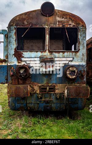 Vieux train électrique rouillé à unités multiples mis hors service et abandonné sur voie ferrée sur un terrain herbeux vert Banque D'Images