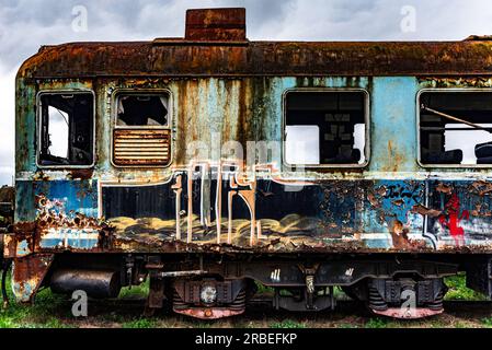 Vieux train électrique rouillé à unités multiples mis hors service et abandonné sur voie ferrée sur un terrain herbeux vert Banque D'Images