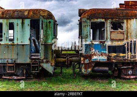 Vieux train électrique rouillé à unités multiples mis hors service et abandonné sur voie ferrée sur un terrain herbeux vert Banque D'Images