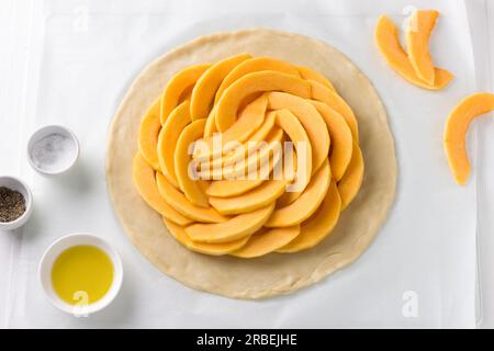 Pâte étalée avec garniture de citrouille entourée d'épices et d'huile d'olive sur un fond en bois blanc, vue de dessus Banque D'Images