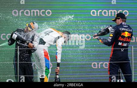 De gauche à droite, Lewis Hamilton de Mercedes, Lando Norris de McLaren et Max Verstappen de Red Bull célèbrent avec du champagne sur le podium après le Grand Prix de Grande-Bretagne 2023 à Silverstone, Towcester. Date de la photo : dimanche 9 juillet 2023. Banque D'Images