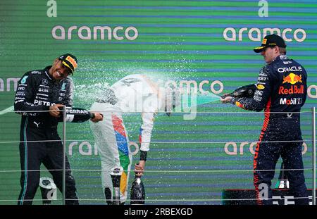 De gauche à droite, Lewis Hamilton de Mercedes, Lando Norris de McLaren et Max Verstappen de Red Bull célèbrent avec du champagne sur le podium après le Grand Prix de Grande-Bretagne 2023 à Silverstone, Towcester. Date de la photo : dimanche 9 juillet 2023. Banque D'Images