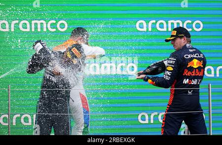 De gauche à droite, Lewis Hamilton de Mercedes, Lando Norris de McLaren et Max Verstappen de Red Bull célèbrent avec du champagne sur le podium après le Grand Prix de Grande-Bretagne 2023 à Silverstone, Towcester. Date de la photo : dimanche 9 juillet 2023. Banque D'Images