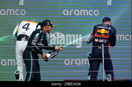 De gauche à droite, Lando Norris de McLaren, Lewis Hamilton de Mercedes et Max Verstappen de Red Bull célèbrent avec du champagne sur le podium après le Grand Prix de Grande-Bretagne 2023 à Silverstone, Towcester. Date de la photo : dimanche 9 juillet 2023. Banque D'Images