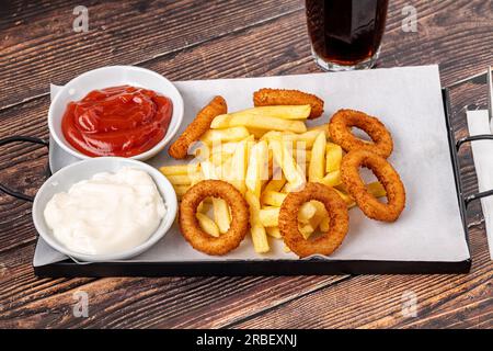 Rondelles d'oignon et frites avec ketchup et mayonnaise sur table en bois Banque D'Images