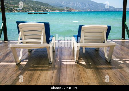 Chaises longues blanches vides avec coussins bleus prêts pour les invités sur la jetée en bois avec vue imprenable sur la mer Banque D'Images